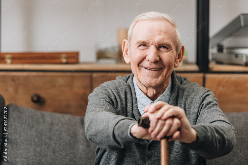 cheerful pensioner smiling and holding walking cane at home - obrazy, fototapety, plakaty 