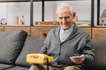 Wall Mural - smiling retired man holding smartphone and old phone at home