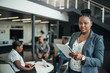 © JonoErasmus - Portrait of a confident black businesswoman using her tablet looking into the camera with all african american team in the background