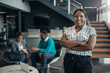 © JonoErasmus - Portrait of a confident black businesswoman smiling with her arms crossed and all african team in the background
