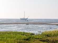 People Looking For Shellfish In Mudflats And Dried Out Sailboat At Low Tide, Waddensea Near Schiermonnikoog, Netherlands