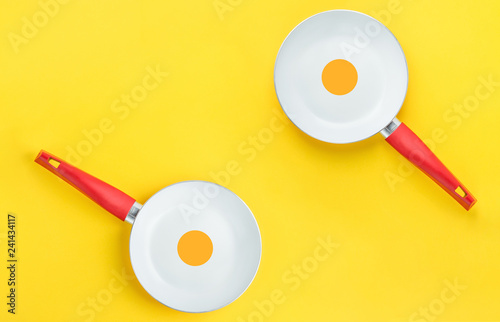 Fotografie, Obraz Couple of symmetric white ceramic frying pans with red handle on bright yellow background
