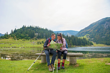 Wall Mural - Hiking couple. Young couple with backpacks looking at the map beside lake