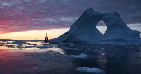 Wall Mural - little red sailboat cruising among floating icebergs in disko bay glacier during midnight sun season