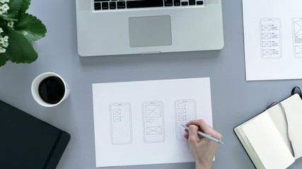 Web designer at work. Graphic designer. Mobile application design. Designer desk. UX, UI design. Thumbnails of a mobile application sketches. Laptop, sketchbook, pencil on the table.