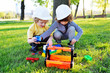 © Evgeniy Kalinovskiy - two small cute children in building helmets play in workers or builders with toy tools in a park on the grass.