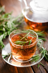 Sticker - Rosemary tea in glass tea cup on rustic wooden table closeup. Herbal vitamin tea.