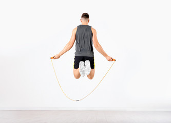 Wall Mural - Sportive man training with jump rope in light room