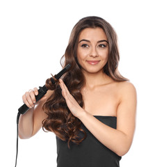 Wall Mural - Beautiful woman using curler on her shiny wavy hair against white background