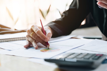 Close up of businessman or accountant hand holding pencil working on calculator to calculate financial data report, accountancy document and laptop computer at office, business concept