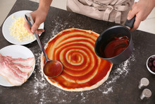 Young Man Applying Sauce On Pizza Dough At Table