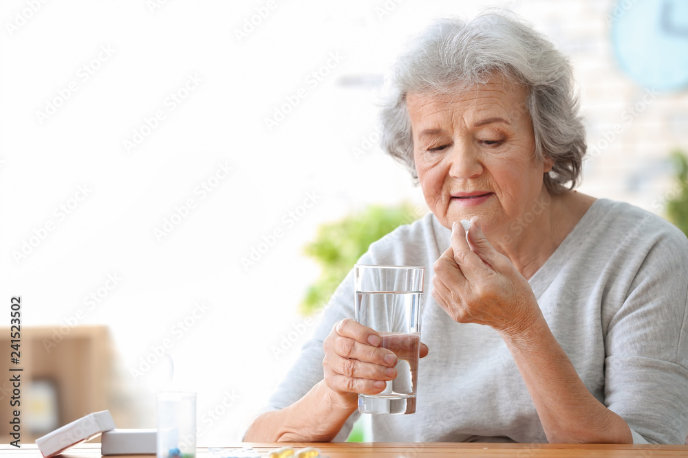 Elderly woman taking pill at home - obrazy, fototapety, plakaty 