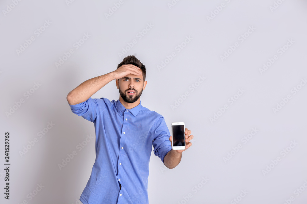 Emotional young man with inoperable mobile phone on white background