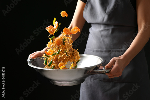 Fotomural Woman cooking tasty Chinese noodles in wok on dark background
