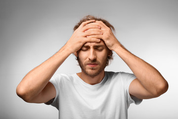 Young man suffering from headache on light background