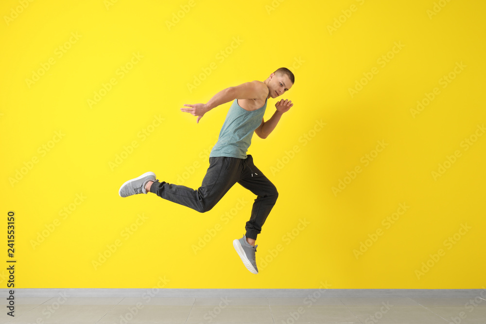 Young male dancer jumping near color wall