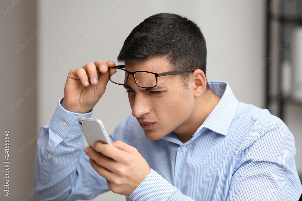 Young man with bad sight trying to read message on screen of mobile phone