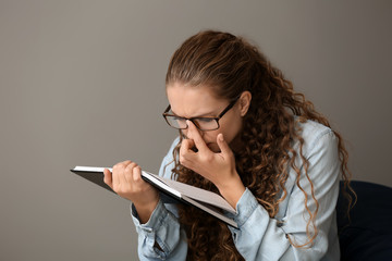 Canvas Print - Young woman with bad sight reading book on grey background