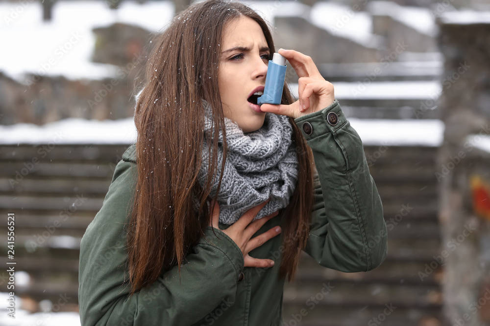 Young woman with inhaler having asthma attack outdoors