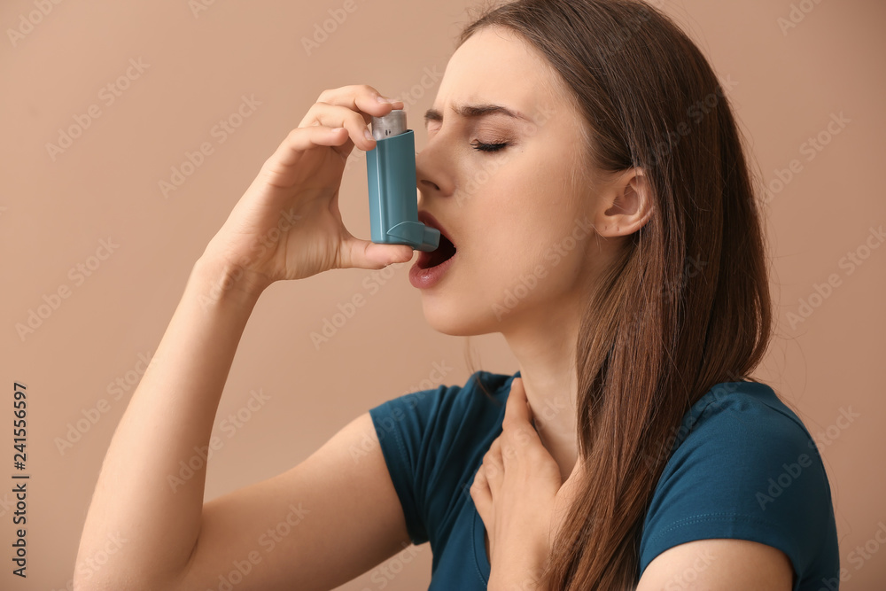 Young woman with inhaler having asthma attack on color background