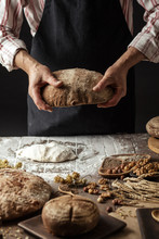 Close Up Of Male Baker Hands Holding Freshly Baked Organic Bread With A Variety Of Bread And Dough On The Foreground
