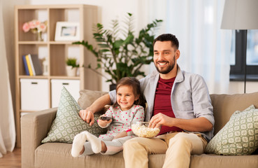 Canvas Print - family, fatherhood and people concept - happy father and daughter with popcorn watching tv at home