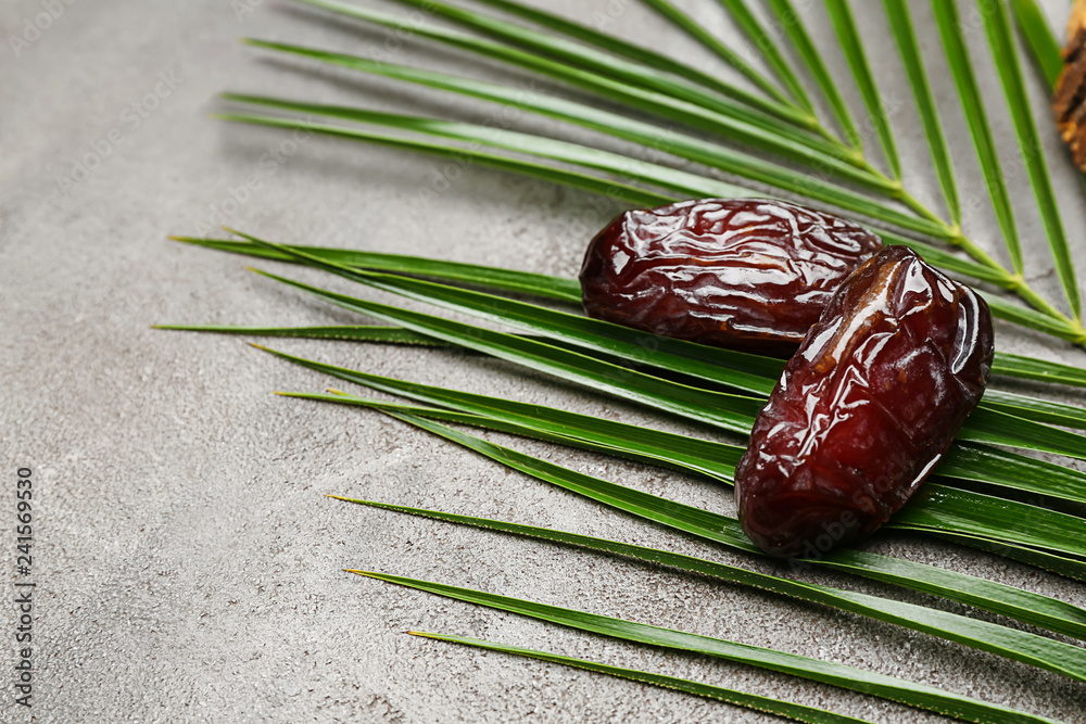 Sweet dried dates and palm leaf on grey background