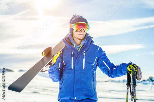 Fotomural Skier ready holding skiing equipment with sun back light on ski slope