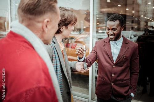 Fotografia, Obraz Dark-haired young man taking car keys form smiling sales consultant