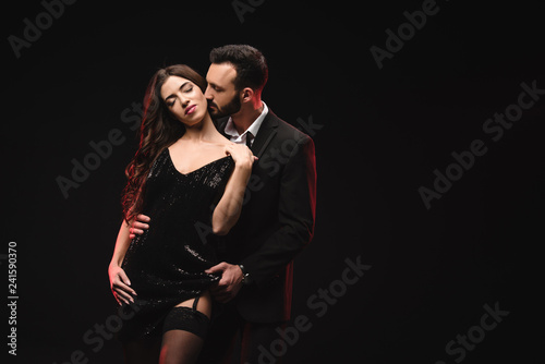 Fototapeta na szkło attractive loving couple in black dress and tuxedo isolated on black