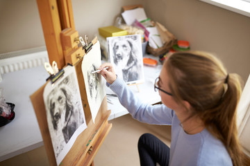 Wall Mural - Rear View Of Female Teenage Artist Sitting At Easel Drawing Picture Of Dog From Photograph In Charcoal