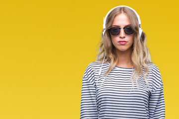 Poster - Beautiful young blonde woman wearing headphones and sunglasses over isolated background with serious expression on face. Simple and natural looking at the camera.