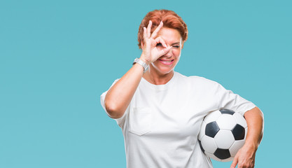 Canvas Print - Atrractive senior caucasian redhead woman holding soccer ball over isolated background with happy face smiling doing ok sign with hand on eye looking through fingers