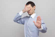 Stop, I Dont Want To See This. Handsome Bristle Businessman In Blue Shirt Standing, Covering His Eyes And Blocking With Hands Stop Gesture . Indoor Studio Shot, Isolated On Grey Background Copyspace.