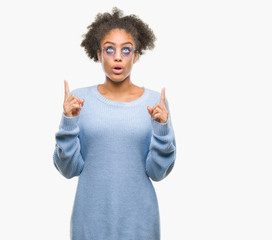 Young afro american woman wearing glasses over isolated background amazed and surprised looking up and pointing with fingers and raised arms.