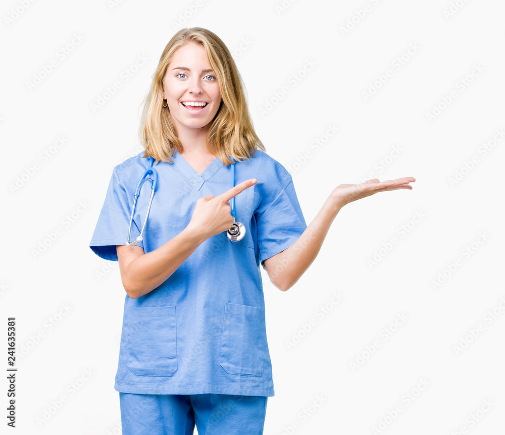 Beautiful young doctor woman wearing medical uniform over isolated background amazed and smiling to the camera while presenting with hand and pointing with finger.
