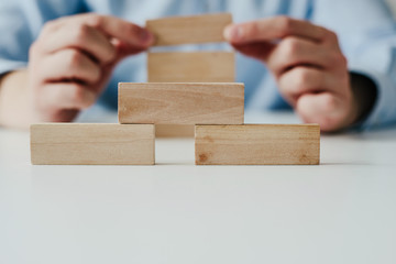 Wall Mural - Businessman in a blue shirt arranges wooden jigsaw blocks. The man arranges empty blocks one on top of the other. Different concepts to supplement with content. Business concept, HR.