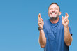 © Krakenimages.com - Middle age hoary senior man over isolated background smiling crossing fingers with hope and eyes closed. Luck and superstitious concept.