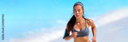 Healthy fit active Asian woman on beach run wearing technology wearable tech device smartphone holder and earphones listening to music motivation on summer workout -banner panorama.