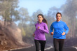 © Maridav - Runners training outside running on road - Two athletes couple jogging in nature wearing sportswear clothing for cold morning fog weather - autumn exercise. Sports lifestyle.