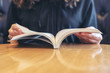 Closeup image of a woman holding and reading a book on wooden table