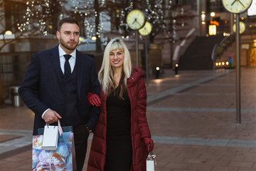 The elegant young couple going by the street with shopping bags after good shopping