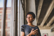 © ReeldealHD images - Young african american female looking out of window in loft apartment holding smartphone