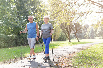 Happy senior couple with hiking poles walking in park