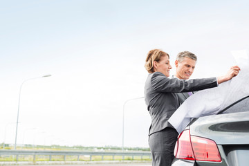 Mature business colleagues analyzing map outside car against sky