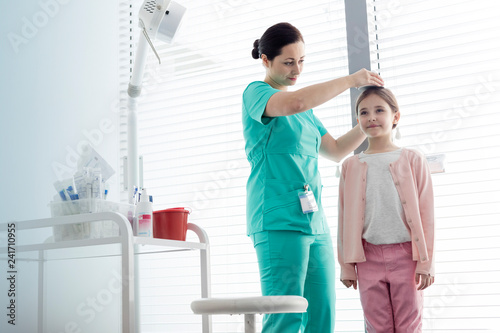 Cuadros en Lienzo Nurse measuring height of girl against window at examination room