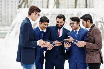 Group of five indian businessman in suits posed outdoor in winter day at Europe, looking on phones and disscus.