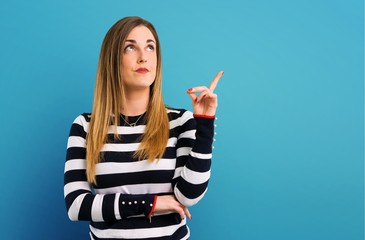 Blonde youn girl pointing with the index finger a great idea on blue background