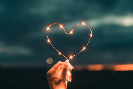 simbolo del cuore fatto da una striscia di luci led tenuto da una mano di una ragazza di fronte al c
