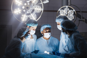 Poster - Surgeons team during operation process in surgery in a dark background. Surgeons stand up through 10-,12-,15-hour surgeries without food, without bathroom breaks without complaints.